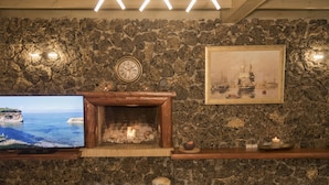 Una pared de piedra con una chimenea, un reloj y un cuadro enmarcado.