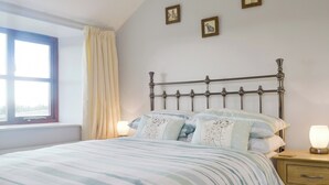 A neatly made bed with striped bedding, a bedside table with a lamp, and a window with curtains. - 3 bedroom accommodation in North Wootton, near Wells (North Wootton, near Wells)