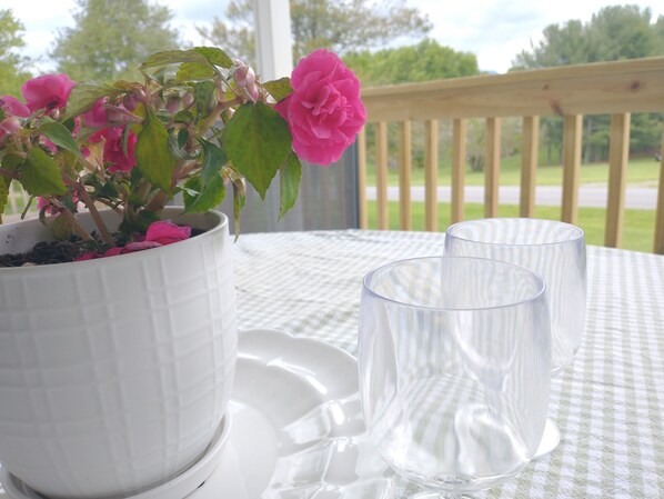 A white potted plant with pink flowers on a table with two clear glasses and white plates.