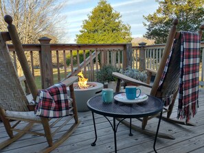 A wooden deck with a rocking chair, a round table, and a fire pit.