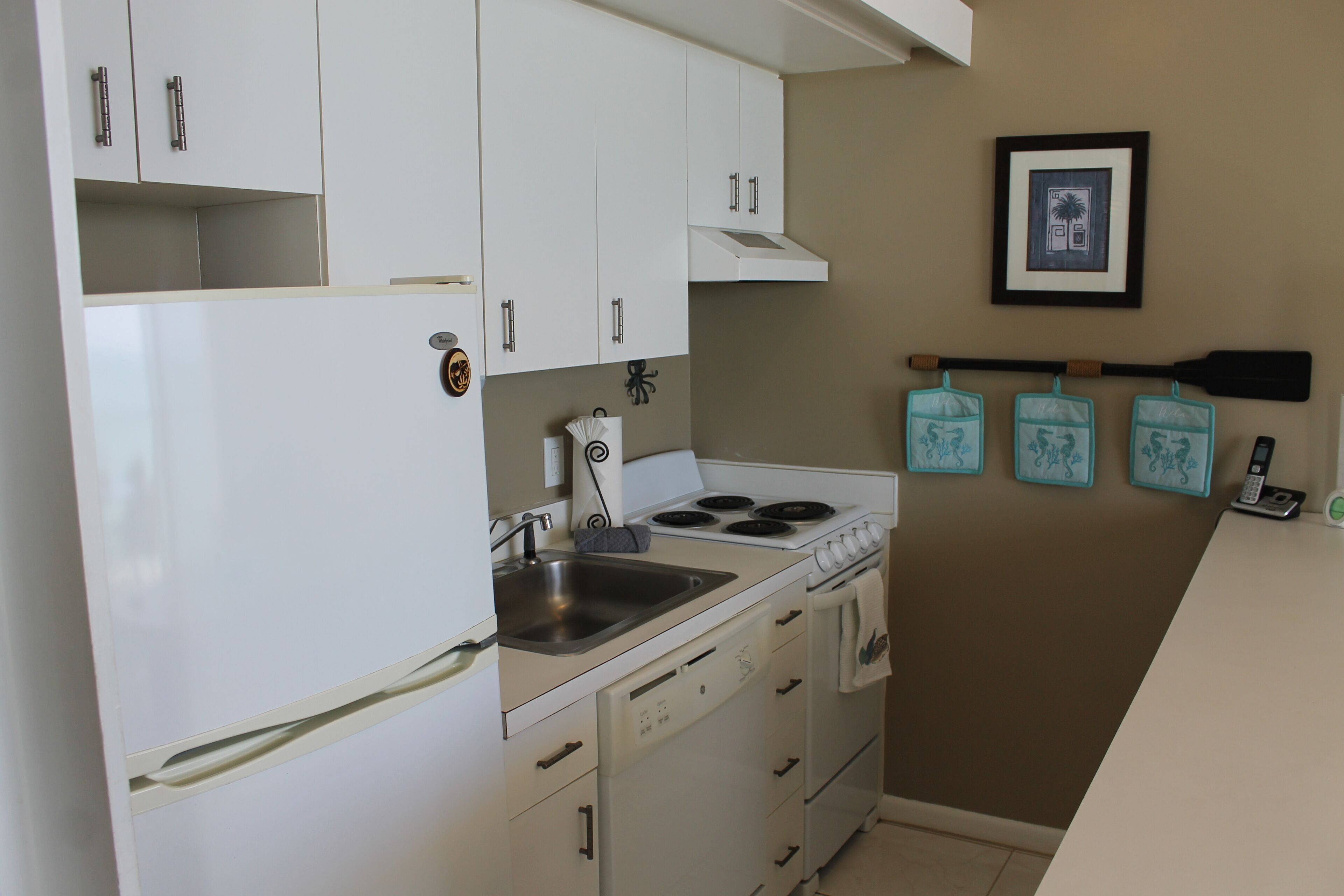 A kitchen with white cabinets, a stove, and a sink. There are three blue kitchen towels hanging on hooks.