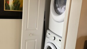 Ett tvättrum med en tvättmaskin och en torktumlare som man matar från framsidan, en vit dörr och en inramad tavla på väggen.