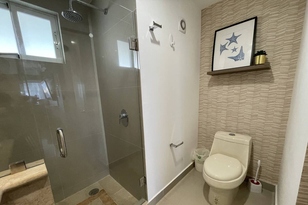 A modern bathroom with a glass-enclosed shower, a toilet, and a shelf with a framed picture.