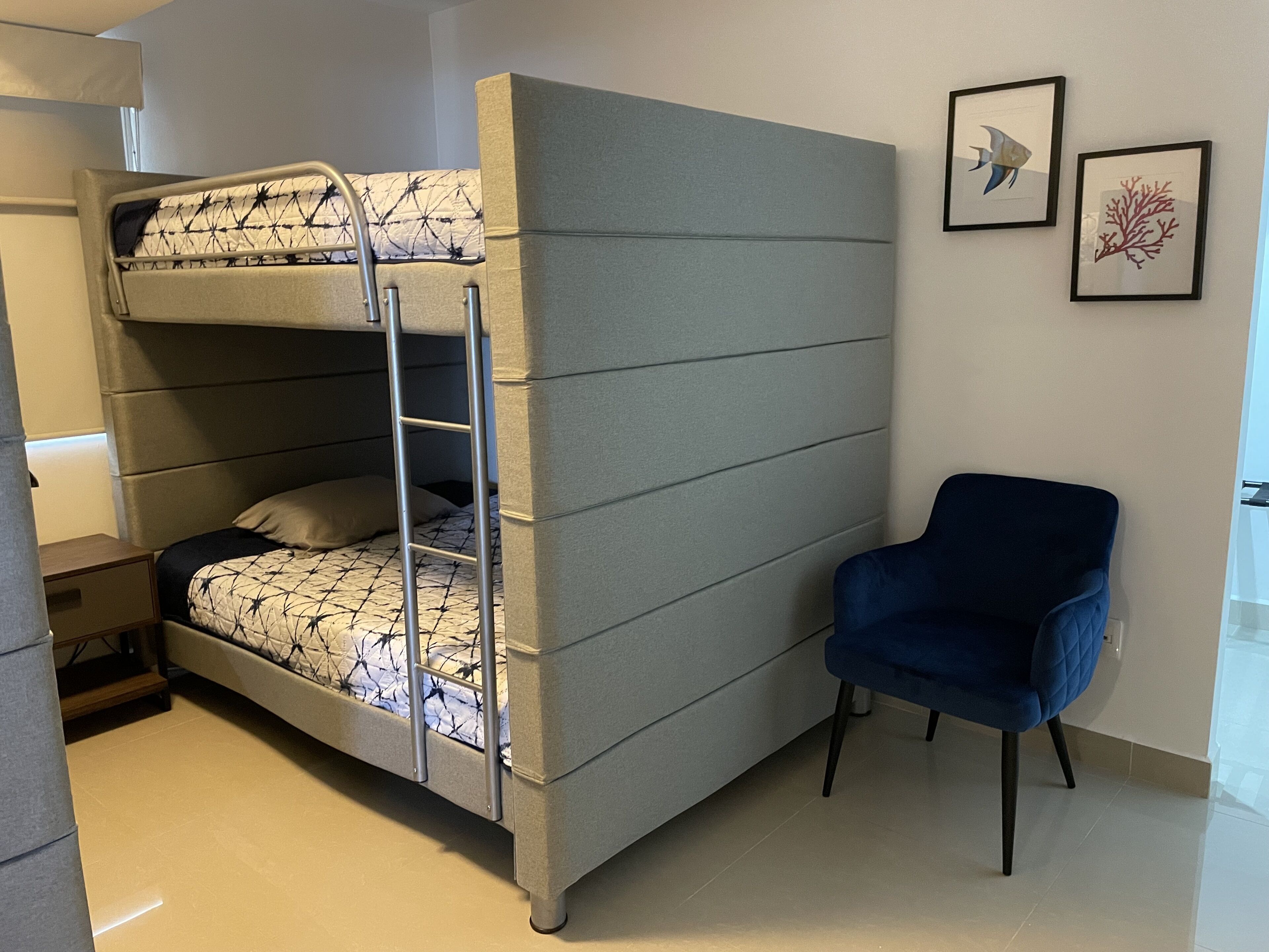 Una cama litera con escalera, una silla azul y dos cuadros en la pared.
