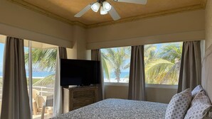 Un dormitorio con cama, televisión y ventanas grandes con cortinas.