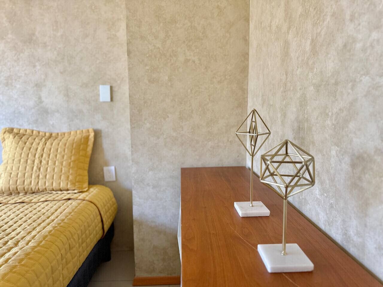 A bedroom with a bed, a wooden nightstand, and two geometric metal sculptures.
