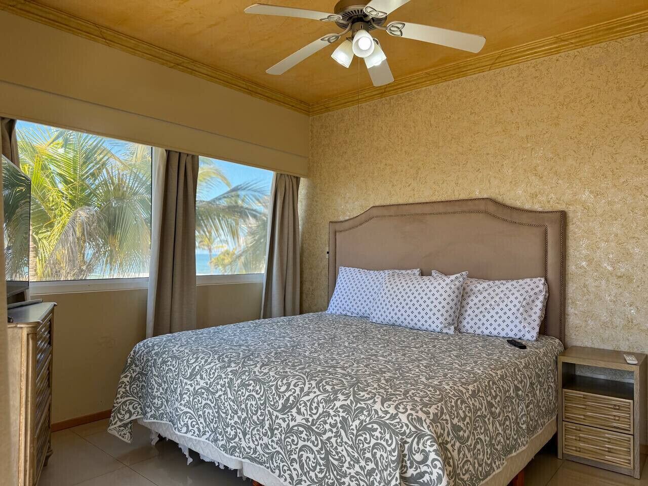 A hotel room with a bed, a ceiling fan, a nightstand, and a window with curtains.