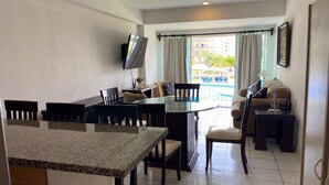 A modern kitchen with granite countertops, a dining area with a glass table, and a living area with a sofa and lamp. - Puesta del Sol (Mazatlán)