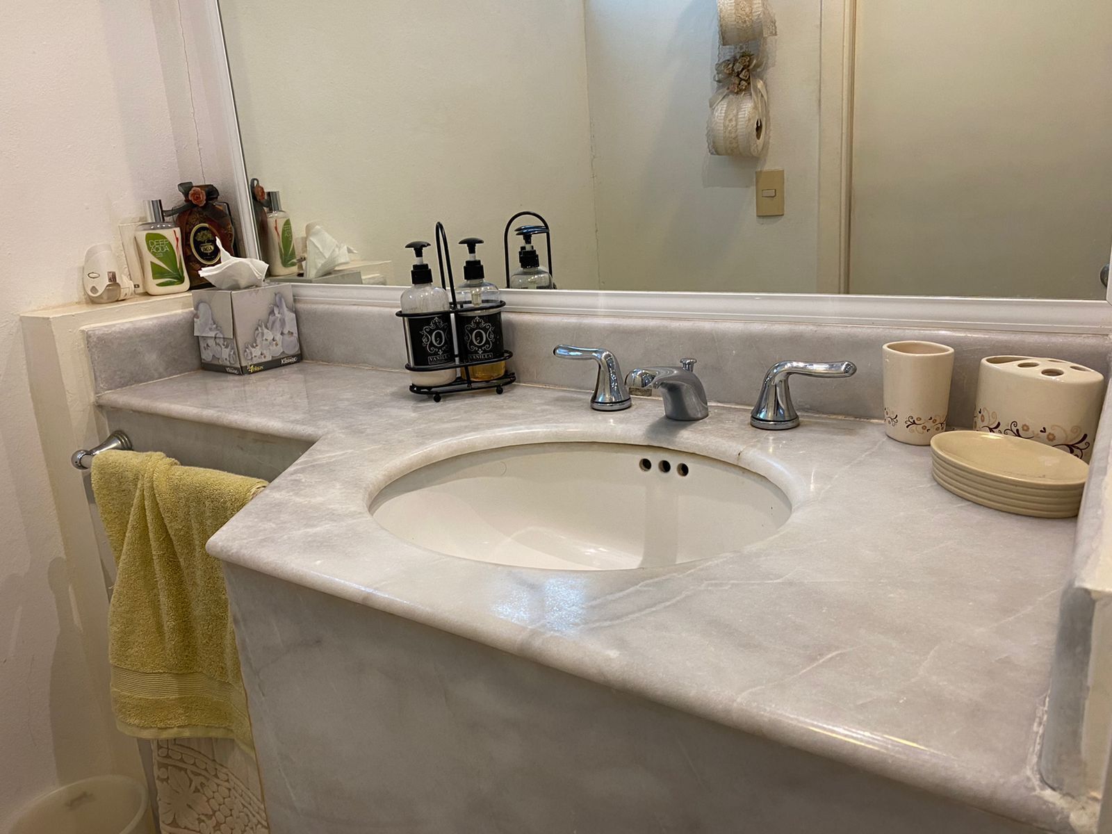 Une salle de bain avec un lavabo en marbre, deux robinets, un miroir et des articles de toilette posés sur le comptoir.