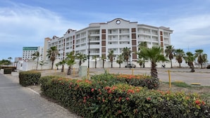 A multi-story hotel with a white facade and red accents, featuring balconies and a parking area with palm trees. - Puesta del Sol (Mazatlán)