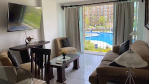 A living room with a TV, a dining table, a sofa, and a view of a pool and buildings. - Puesta del Sol (Mazatlán)