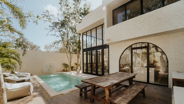 Um pátio moderno ao ar livre com piscina, móveis de madeira e vista para a paisagem circundante.