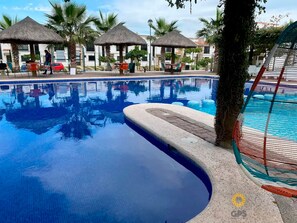 A swimming pool with clear blue water, surrounded by lounge chairs and thatched umbrellas. - Azul Marino (Mazatlán)
