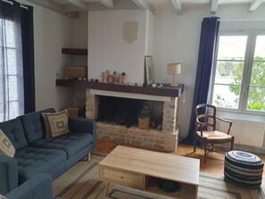 Uma sala de estar aconchegante com lareira, um sofá azul, uma mesa de centro de madeira e uma janela com cortinas.