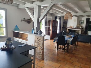 A spacious kitchen with a stone island, a dining area with a blue tablecloth, and a view of the outdoors through a window.
