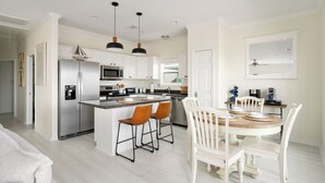 Une cuisine moderne avec des meubles blancs, des appareils en acier inoxydable et un îlot central doté de tabourets de bar.