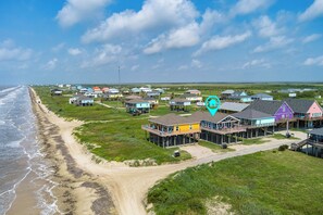 A coastal residential area with houses on stilts, a beach, and a clear sky. - Beachfront Views • Steps to the Sand • Dog Friendly • Sleeps 8 (Bolivar Peninsula)
