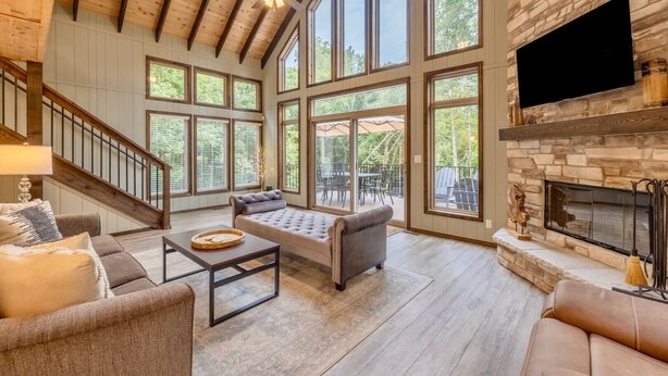 Una sala de estar amplia con techo alto, ventanas grandes, chimenea y escalera.