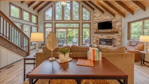 Un salón amplio con chimenea de piedra, ventanas grandes y una escalera de madera.