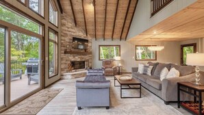 Un salón espacioso con chimenea de piedra, ventanas amplias y un techo alto con vigas a la vista.