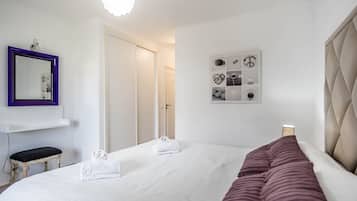 A hotel room with a bed, a bedside table, a mirror, and a wall art piece.