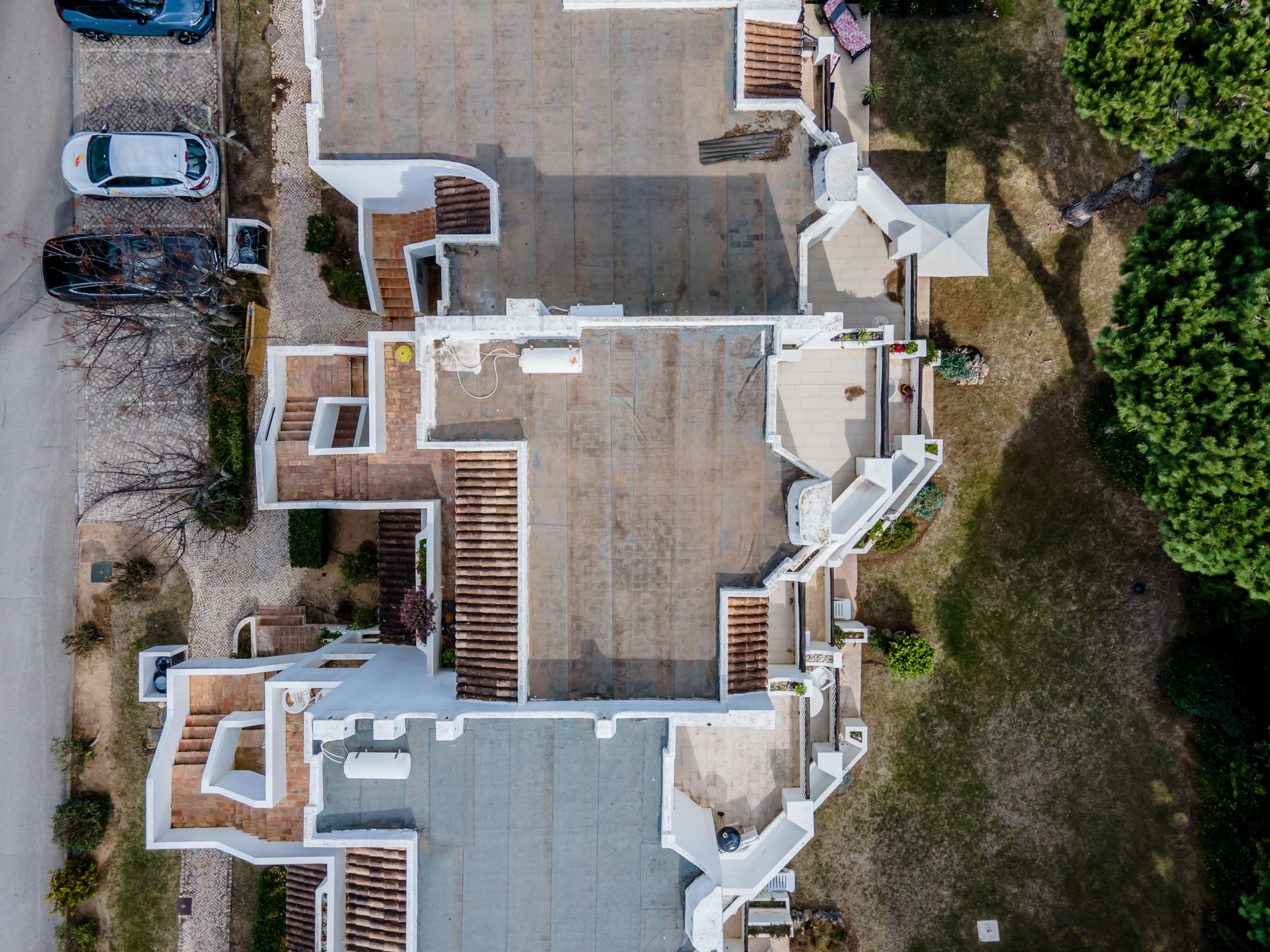 An aerial view of a residential property with a central courtyard, multiple entry points, and a parking area with cars.