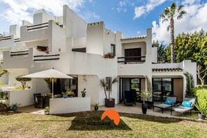 Ein modernes, zweistöckiges Haus mit Terrasse, Sitzgelegenheiten im Freien und Topfpflanzen.