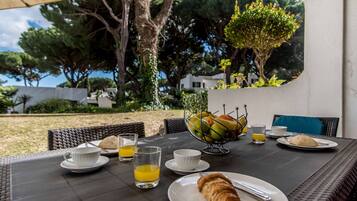 An outdoor dining area with wicker chairs, a table set with plates, glasses, and a fruit bowl.