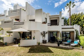 Un edificio moderno de varios pisos con balcones, mobiliario exterior y plantas en macetas.