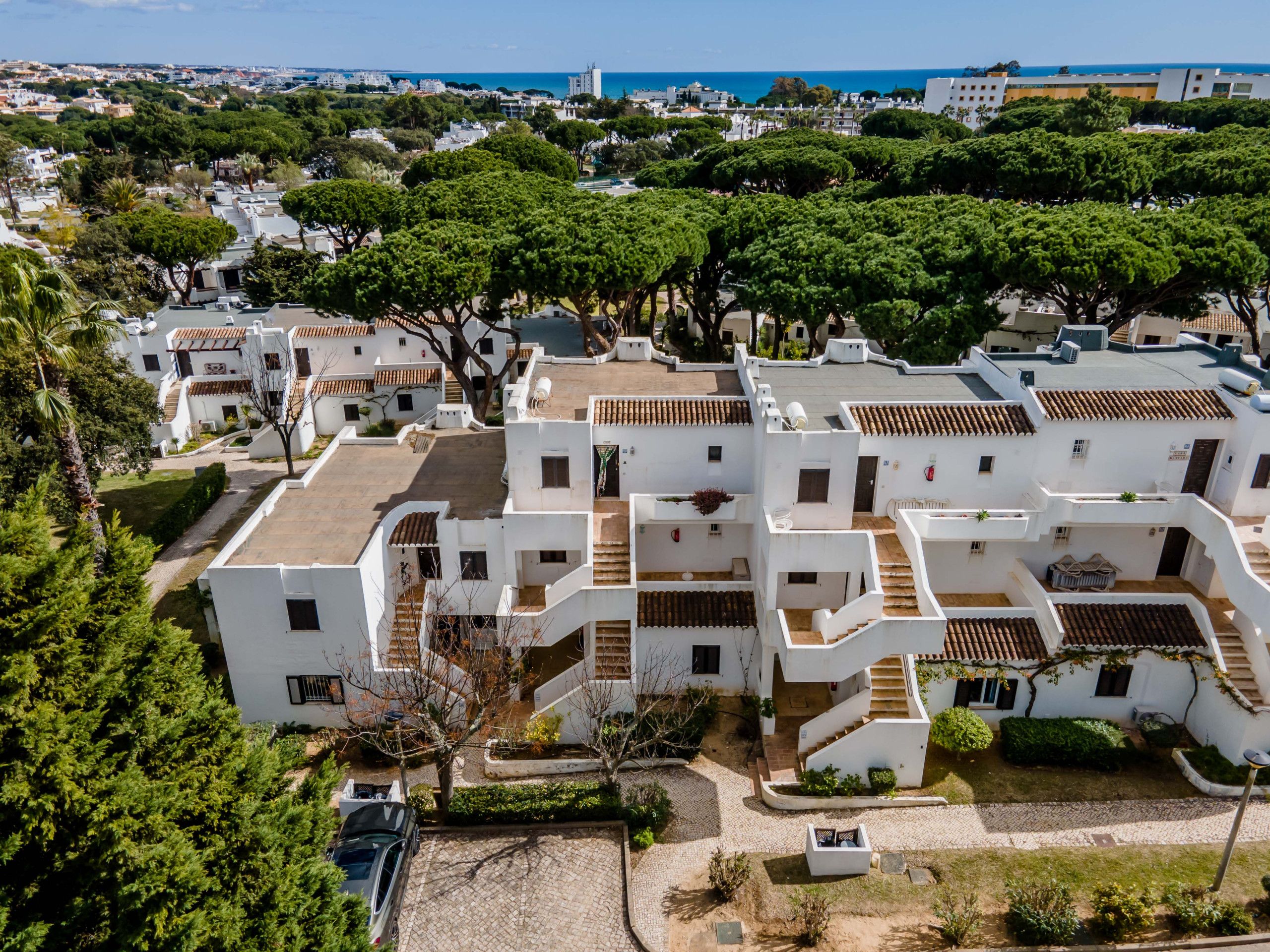 A residential area with white buildings, green trees, and a clear view of the sea.