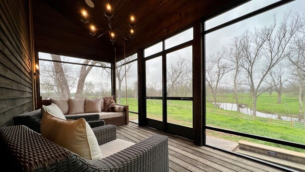 A covered outdoor seating area with wicker furniture and large windows overlooking a grassy landscape. - ELLINGER COUNTRY FARMHOUSE  (Columbus)