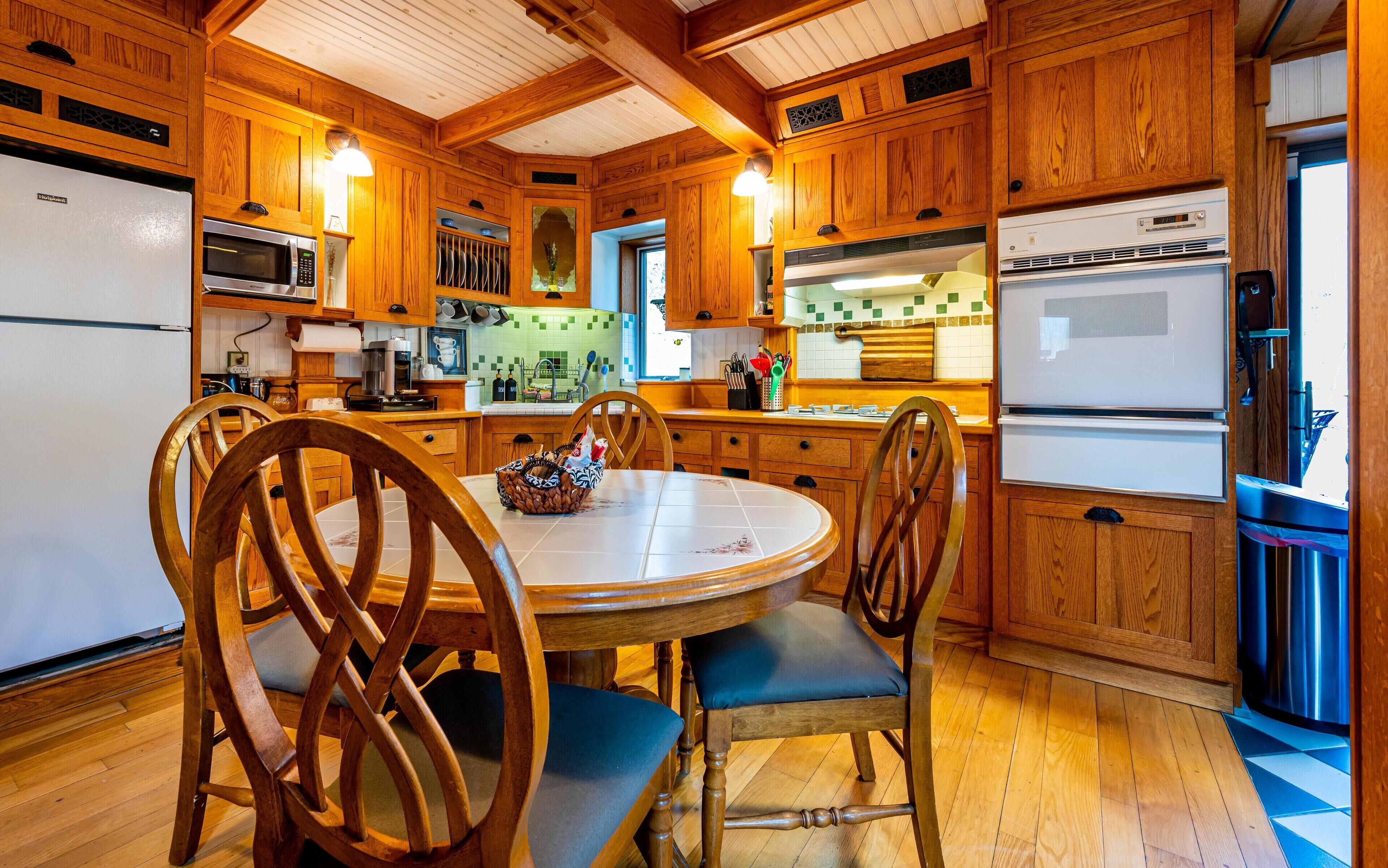 A wooden kitchen with a round dining table, chairs, and various appliances.
