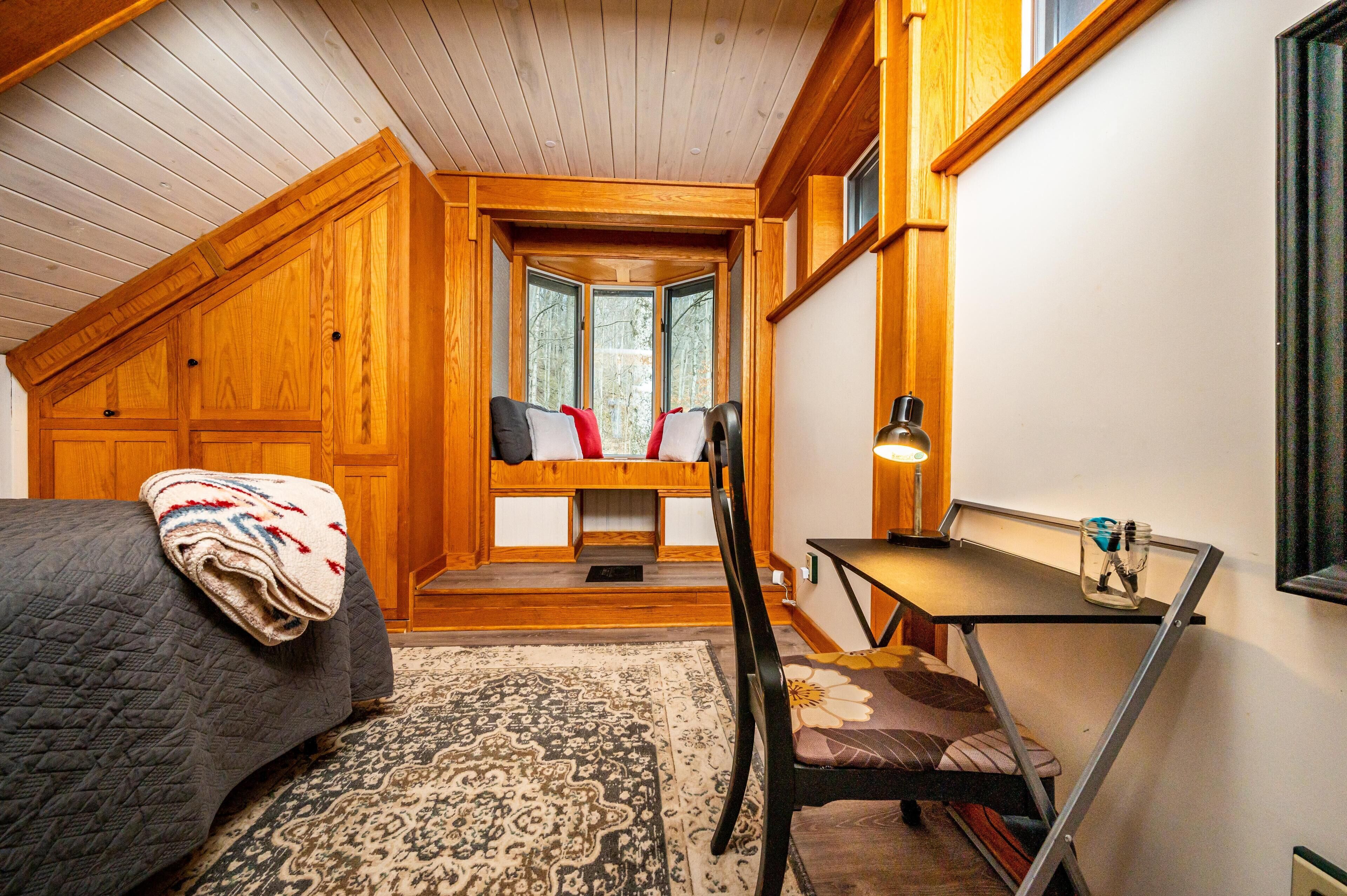 A cozy room with a bed, a desk, and a window overlooking a forest.