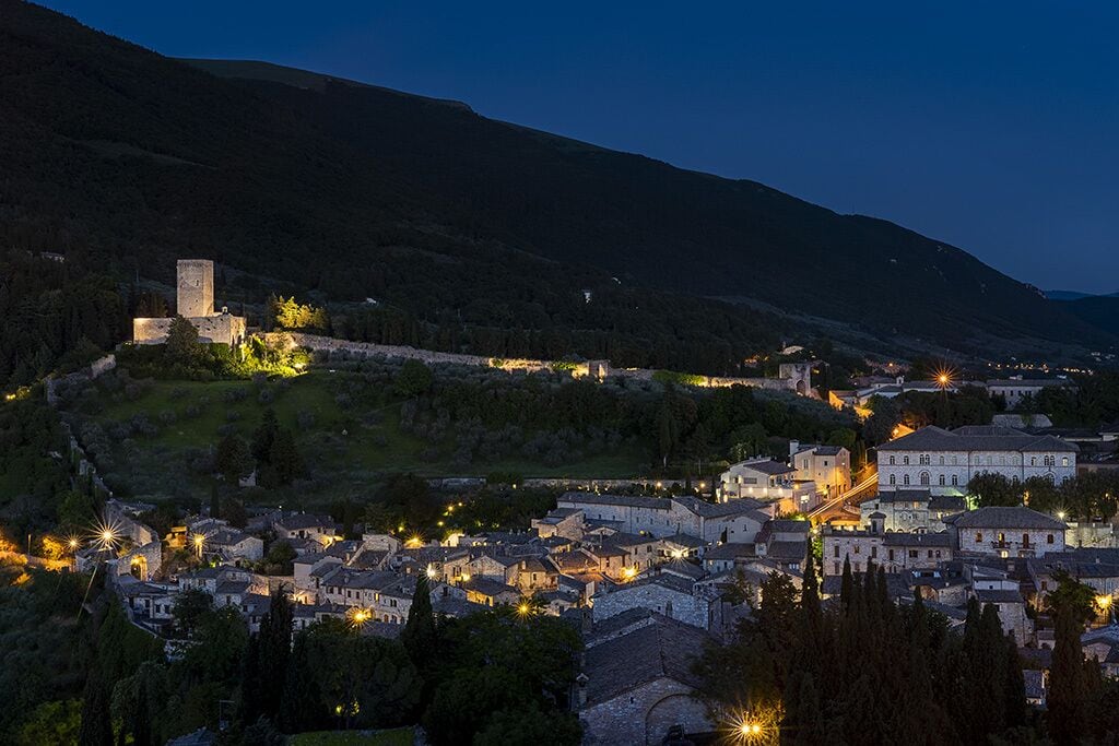 A historic town with medieval architecture, including a prominent tower and well-lit buildings.