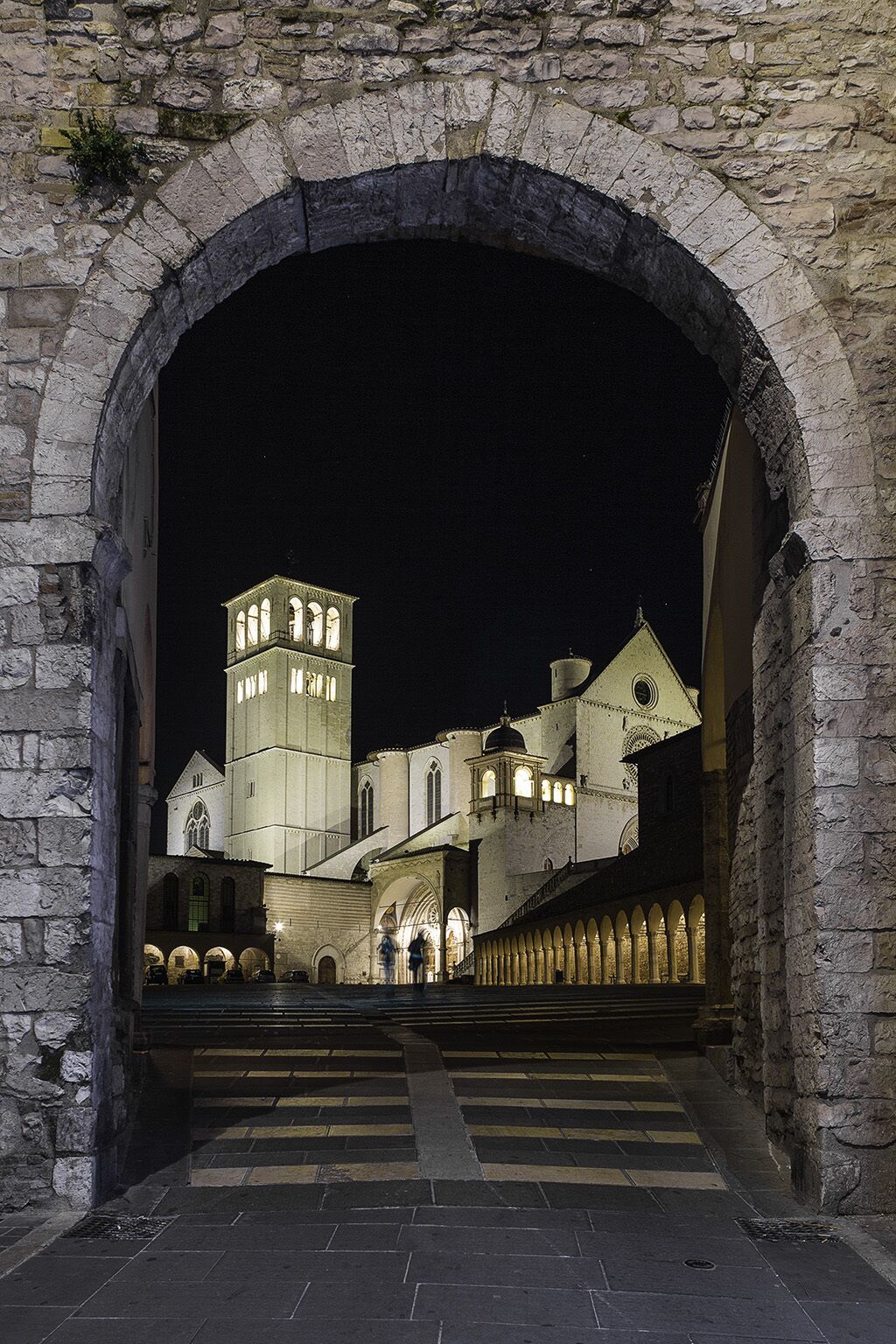 An arched stone gateway leading to a historic building with multiple towers and arches.