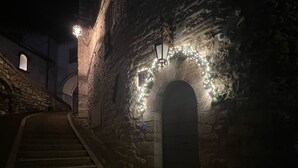 A dimly lit stone staircase leading to an arched doorway, with a lantern and a 'R' sign above it. - C' ERA UNA VOLTA  (Assisi)