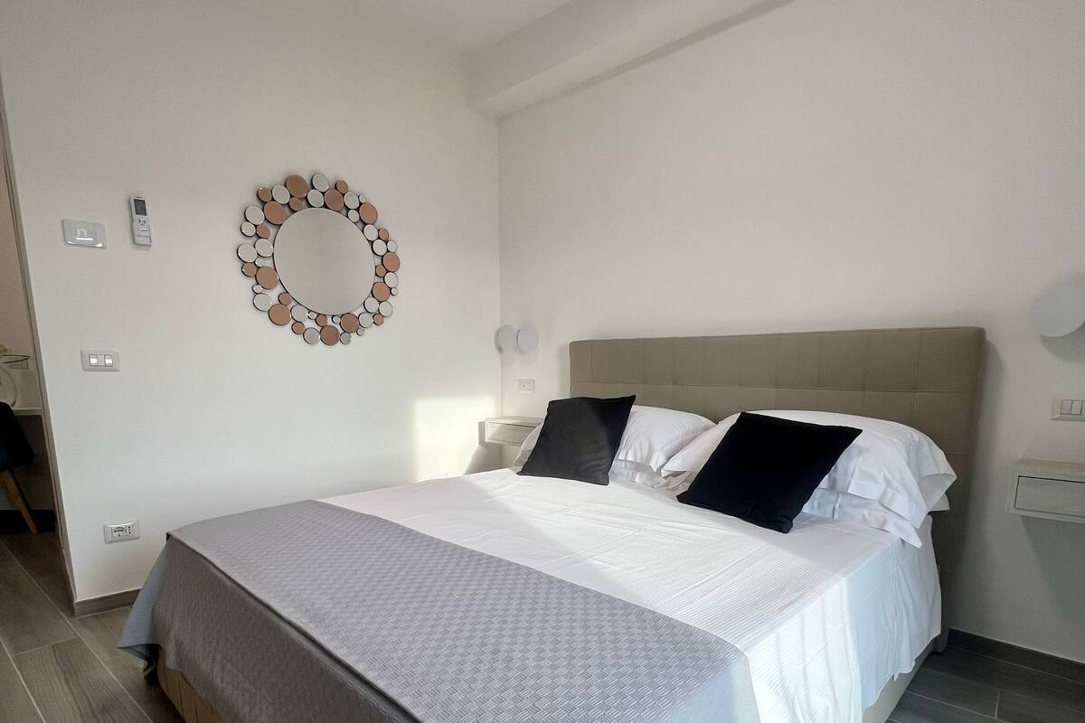 A neatly made bed with a grey and white bedspread, a circular wall decoration, and a modern headboard.