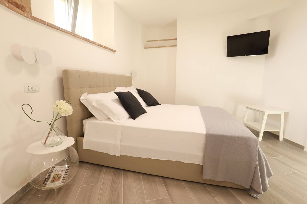 A modern bedroom with a bed, bedside table, and a TV mounted on the wall.