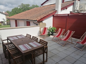 An outdoor patio with a wooden table and chairs, a red and white striped chair, and a potted plant.