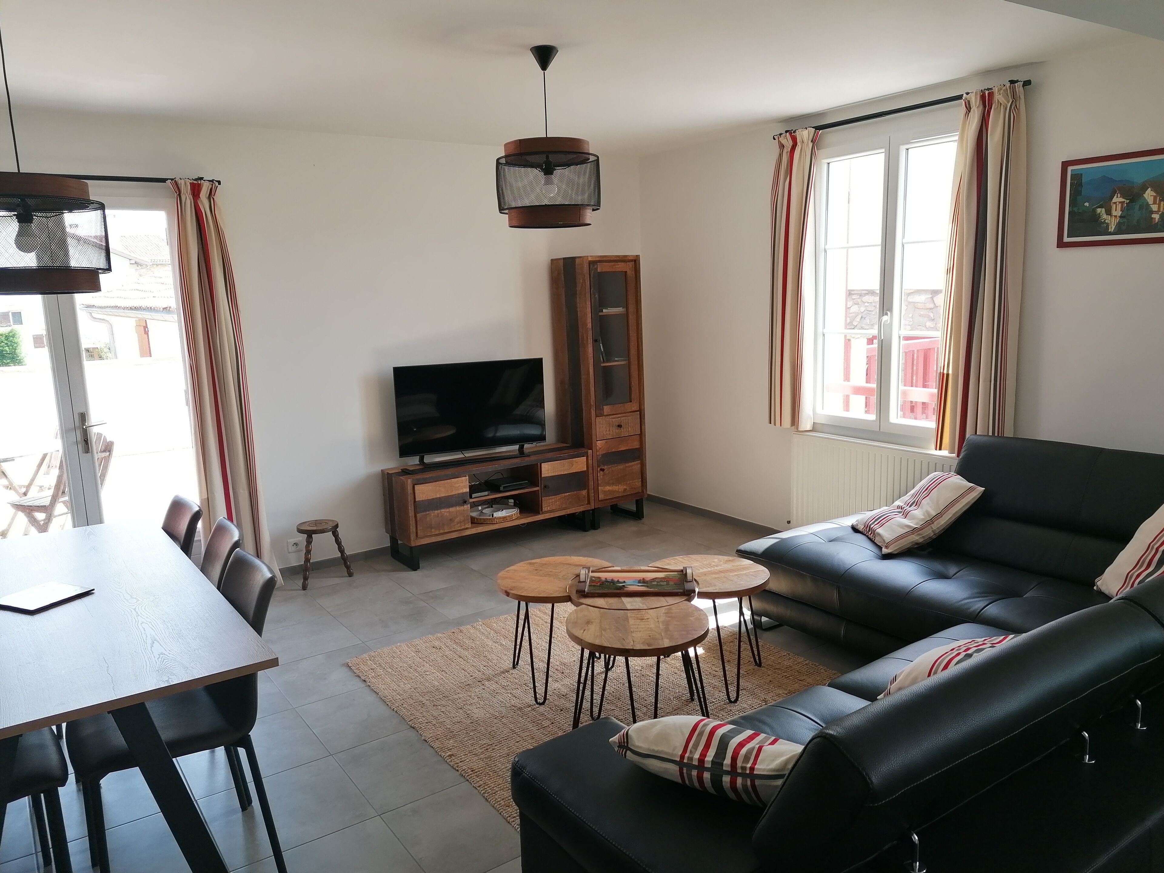 A living room with a sofa, TV, wooden cabinet, dining table, and a view of the outside.