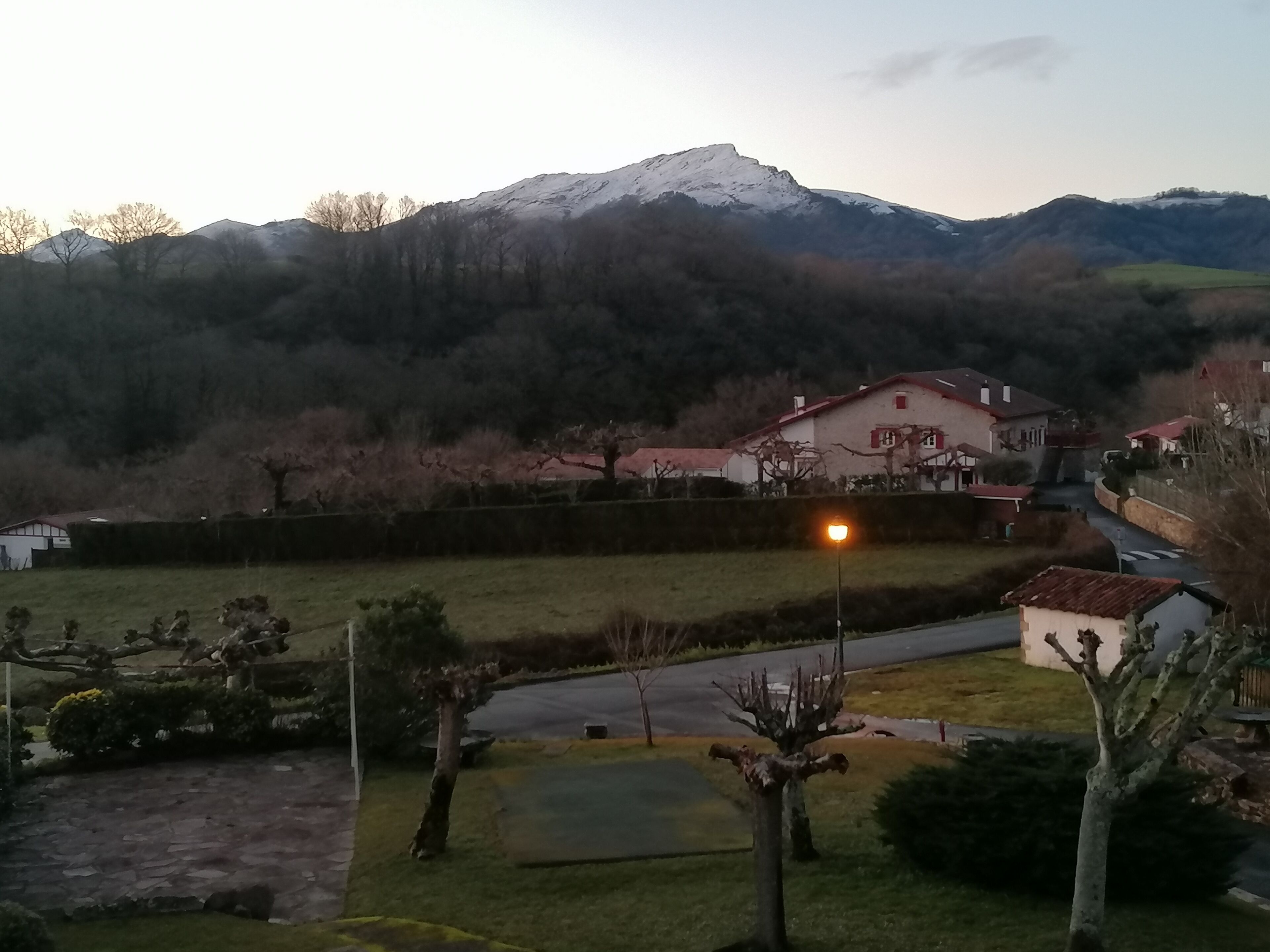 Ländliche Landschaft mit einem Haus, einer Straße und einem Berg im Hintergrund.