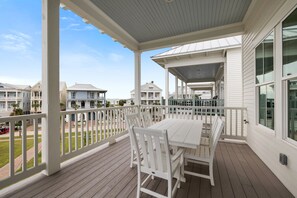 Een overdekt terras met een witte tafel en stoelen, met uitzicht op een woonwijk met meerdere huizen.