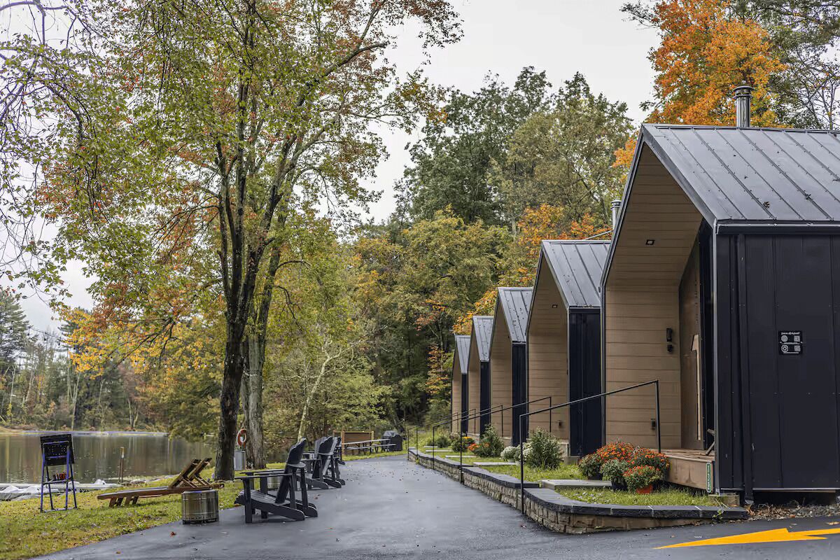 A row of cabins with a paved walkway, a bench, and a small table with chairs.