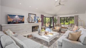A modern living room with a fireplace, comfortable seating, and large windows offering a view of greenery. - Calistoga Wine Ranch Estate (Napa Valley)