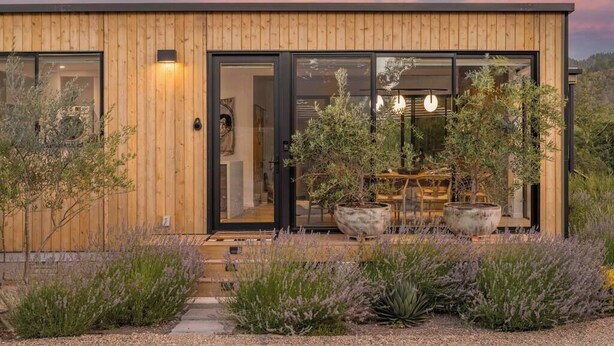 A modern wooden building with large glass doors, a garden with lavender, and a view of the interior. - Calistoga Wine Ranch Estate (Napa Valley)
