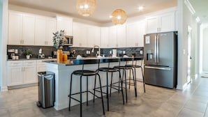A modern kitchen with white cabinets, a stainless steel refrigerator, and a central island with bar stools.