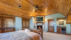 Une chambre avec un grand lit, une cheminée, un plafond en bois et un mur en pierre.