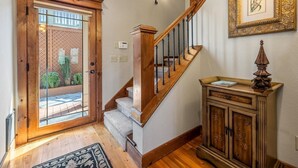 Un escalier en bois avec une rampe, une porte dotée d’un panneau en verre, un luminaire fixé au mur et un tableau encadré.