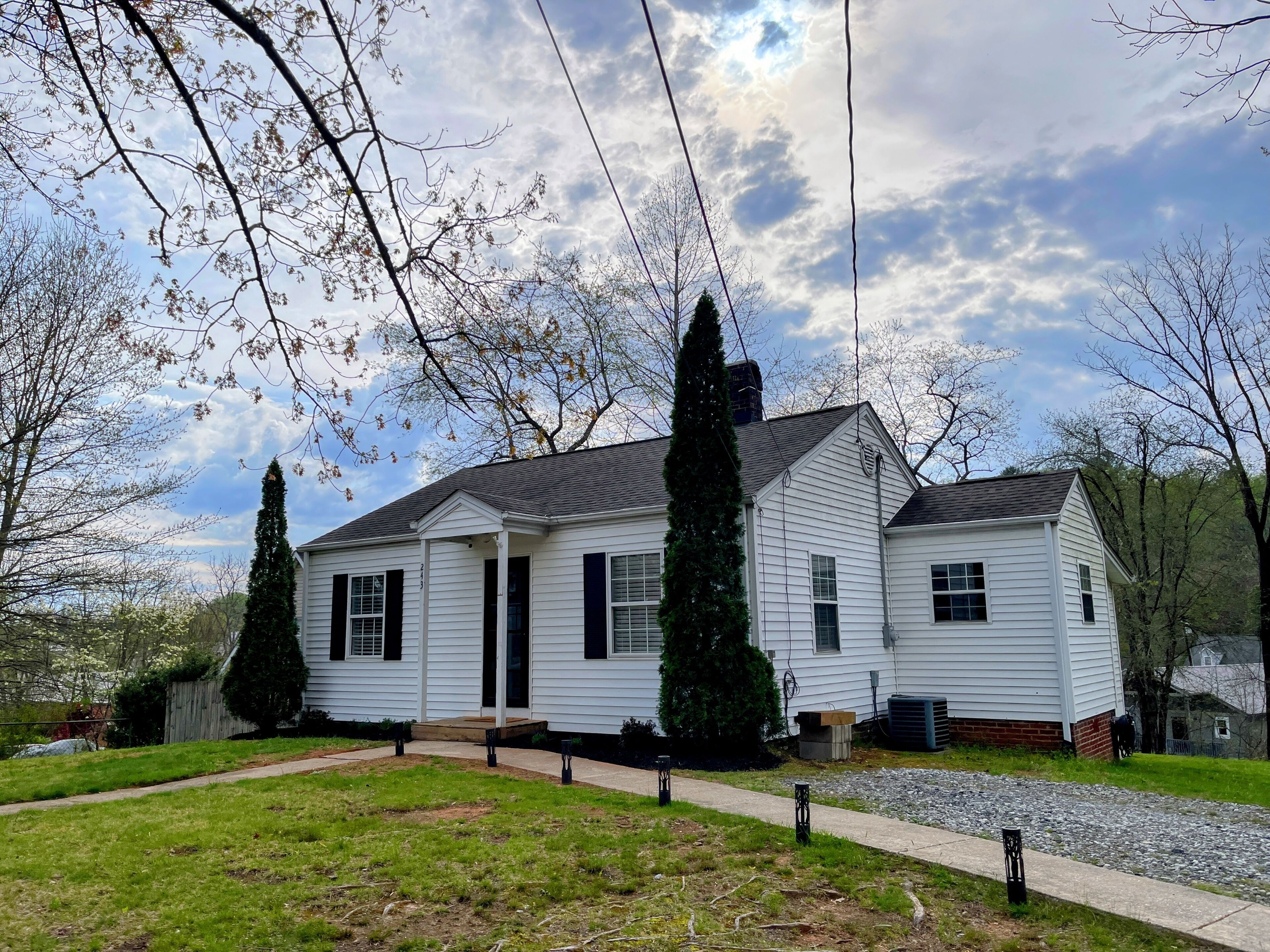 A two-story white house with a front porch, a chimney, and a gravel driveway.
