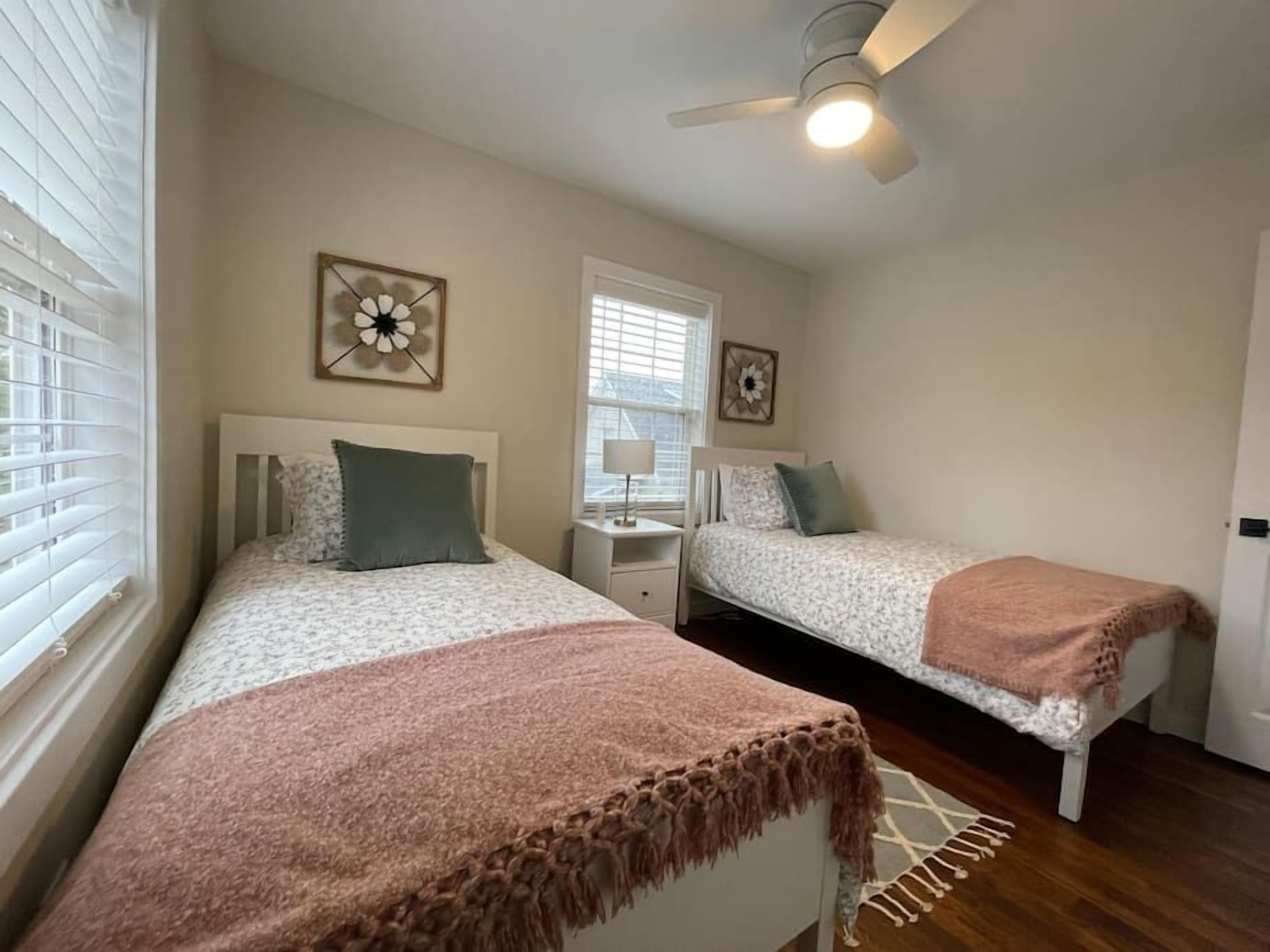 A bedroom with two beds, a ceiling fan, and a window with blinds.